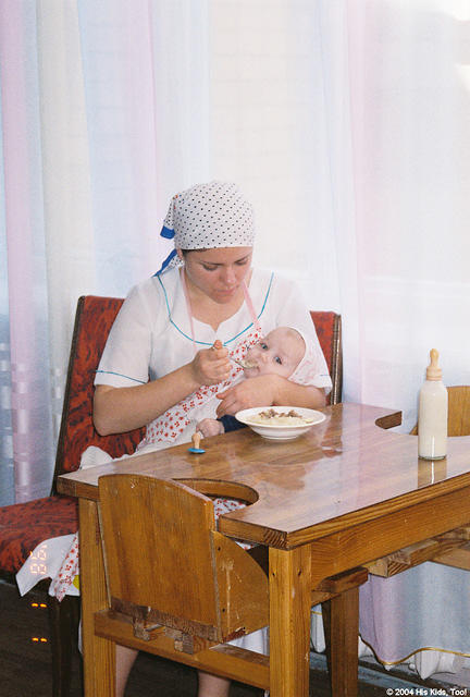 This caregiver is feeding this baby potatoes and a bottle of milk.