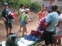 Children stand with bundles of clothes, so many that some just set them down on the bench.
